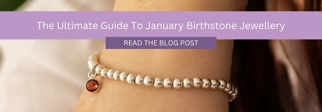 A close-up of a person's wrist adorned with a beaded bracelet featuring a small red gemstone charm. A purple banner with white text overlays the image, reading "The Ultimate Guide To January Birthstone Jewellery" with a button below saying "READ THE BLOG