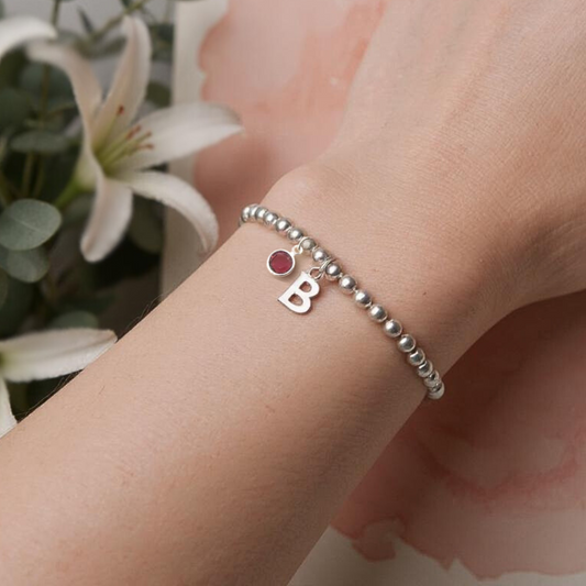 Silver stretch bead bracelet with ruby birthstone and letter charm, letter 'B' is selected in the image.