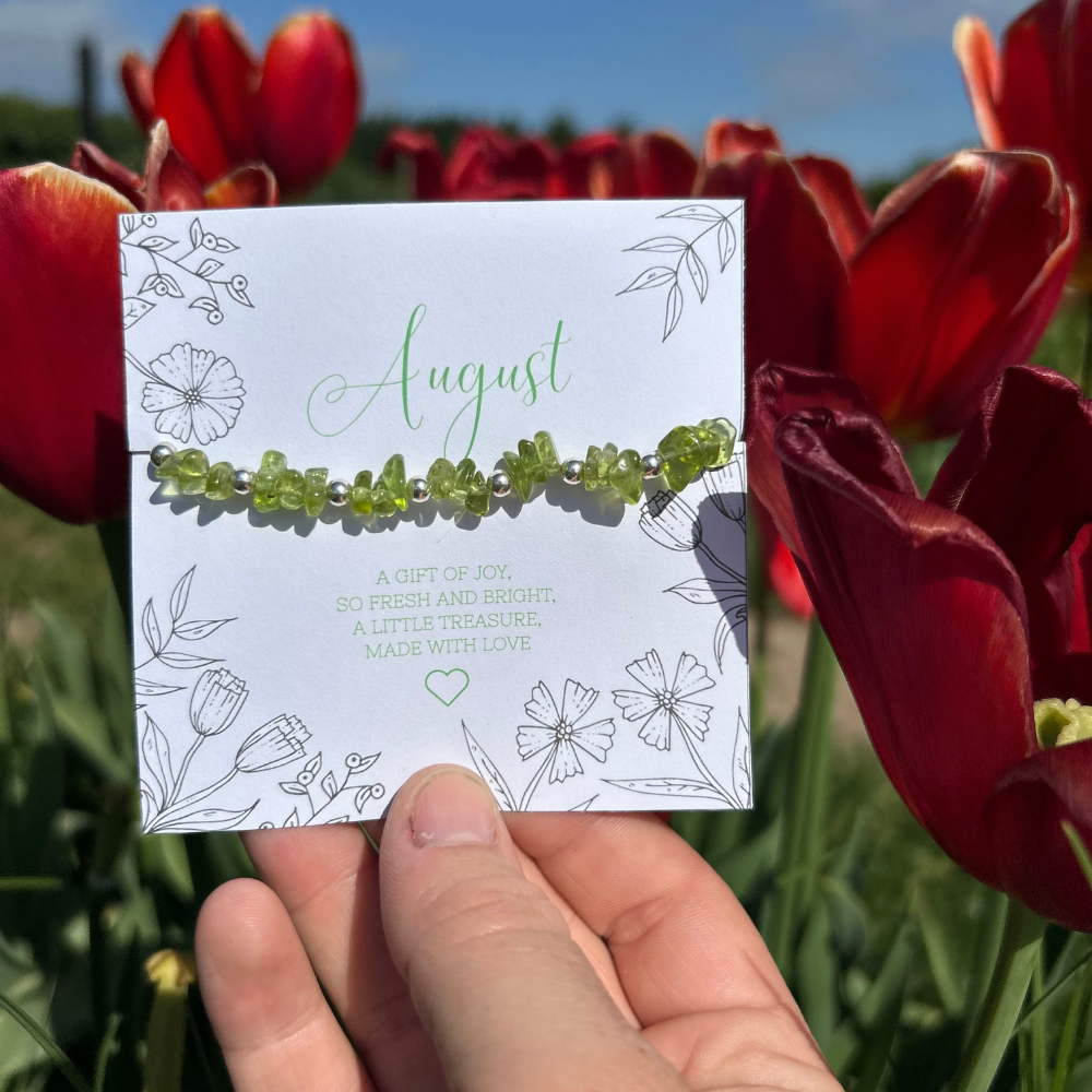 A beautiful peridot crystal bead bracelet, with a floral backdrop and august birthday gift card
