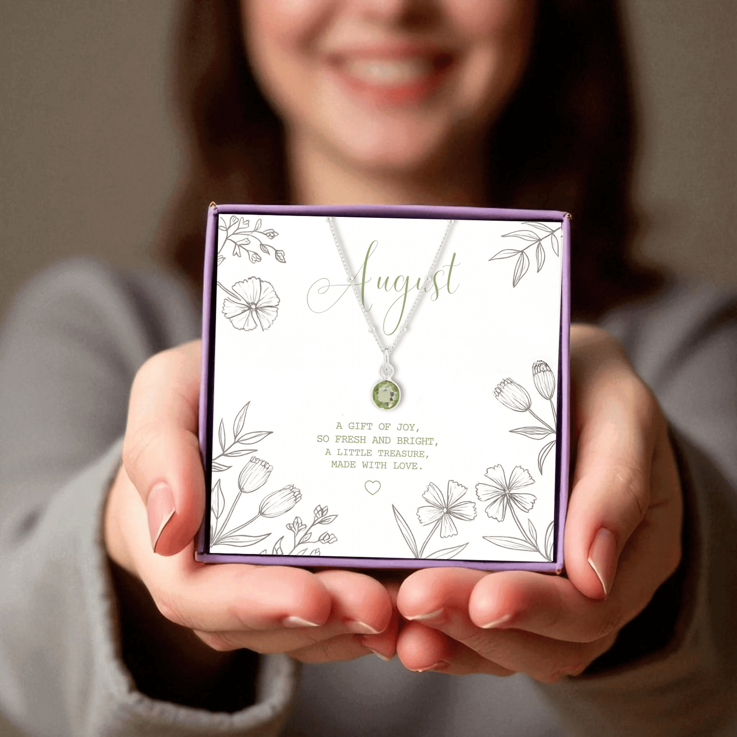August birthstone pendant necklace sitting inside made here with love gift box, in the hands of a young lady.
