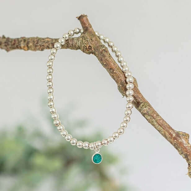 Sterling silver bead bracelet with emerald green charm hanging on a branch– a meaningful gift for May birthdays.