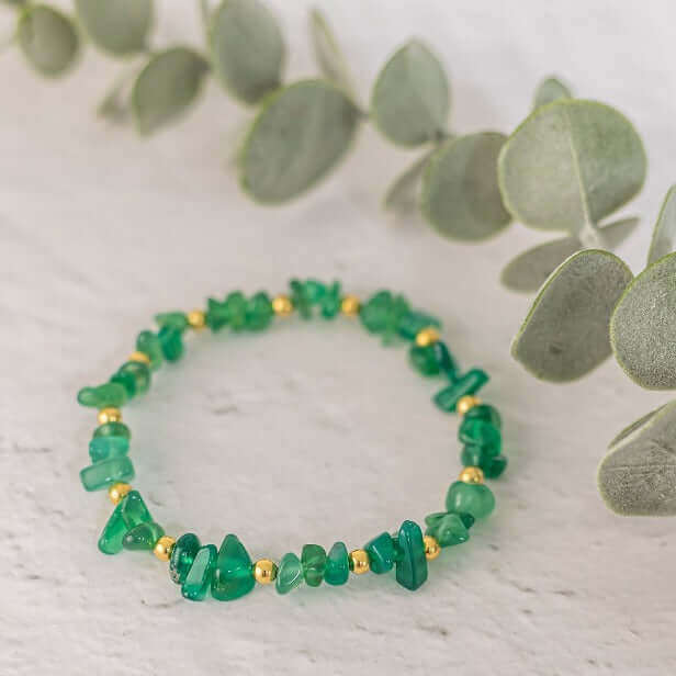 Green agate crystal chip bracelet with gold colour beads styled on a white marble background – handmade stretch bead bracelet for everyday wear.