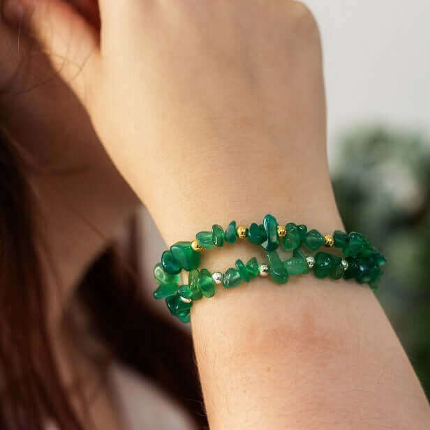Woman wearing two green agate stretch bracelet on wrist, one with silver bead accents, the other with gold– a meaningful crystal chip bracelet and alternative May birthstone piece.