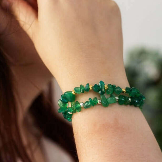 Woman wearing two green agate stretch bracelet on wrist, one with silver bead accents, the other with gold– a meaningful crystal chip bracelet and alternative May birthstone piece.