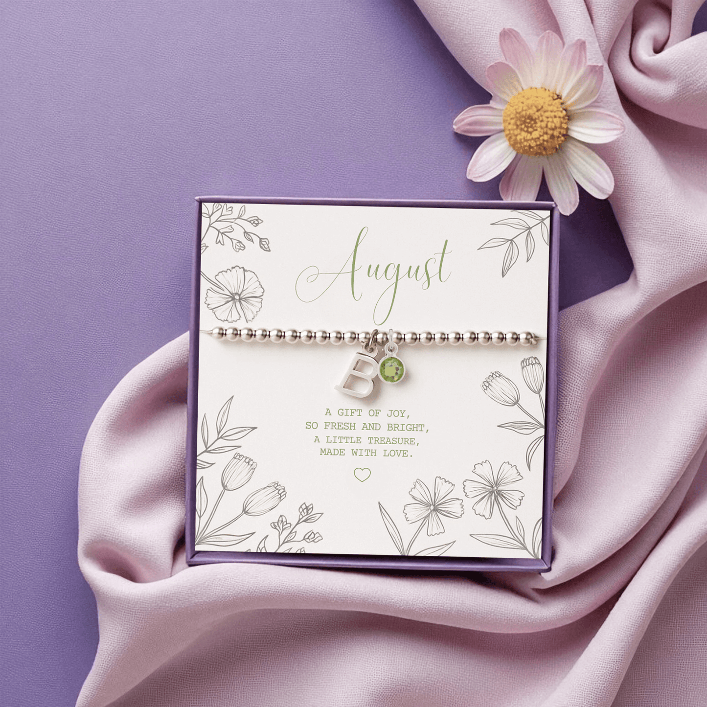 Initial & August Birthstone Bracelet with peridot charm shown on purple satin backdrop beside daisy and ribbon