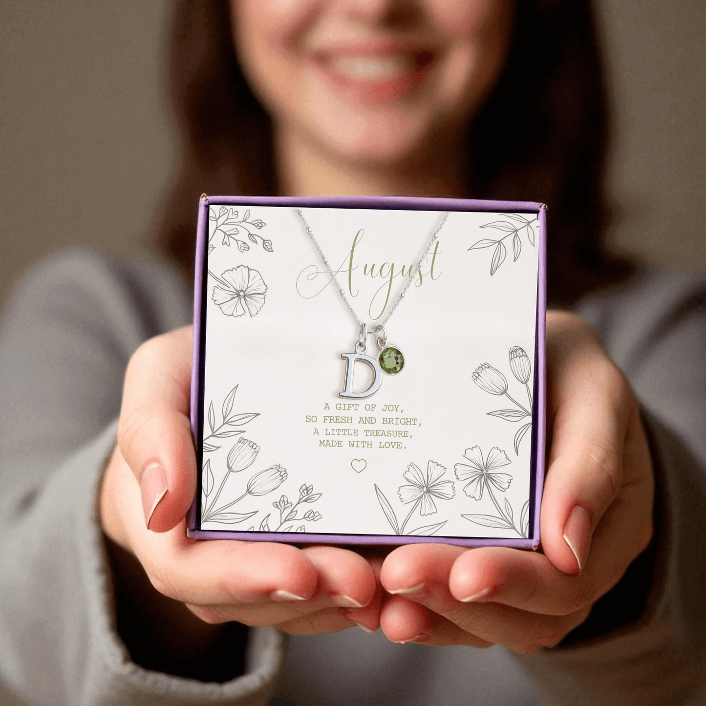 Sterling silver initial and peridot August birthstone necklace presented in a purple gift box with floral card reading “A gift of joy, so fresh and bright”