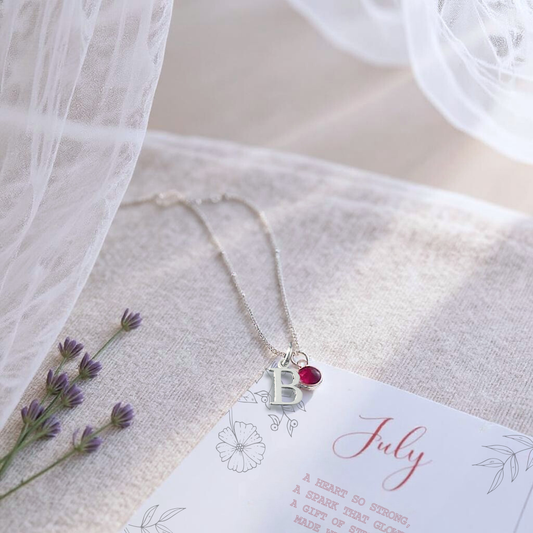 July birthstone and letter necklace shown resting on july birthstone message card. This Ruby birthstone necklace is the perfect personalised gift for a loved one.