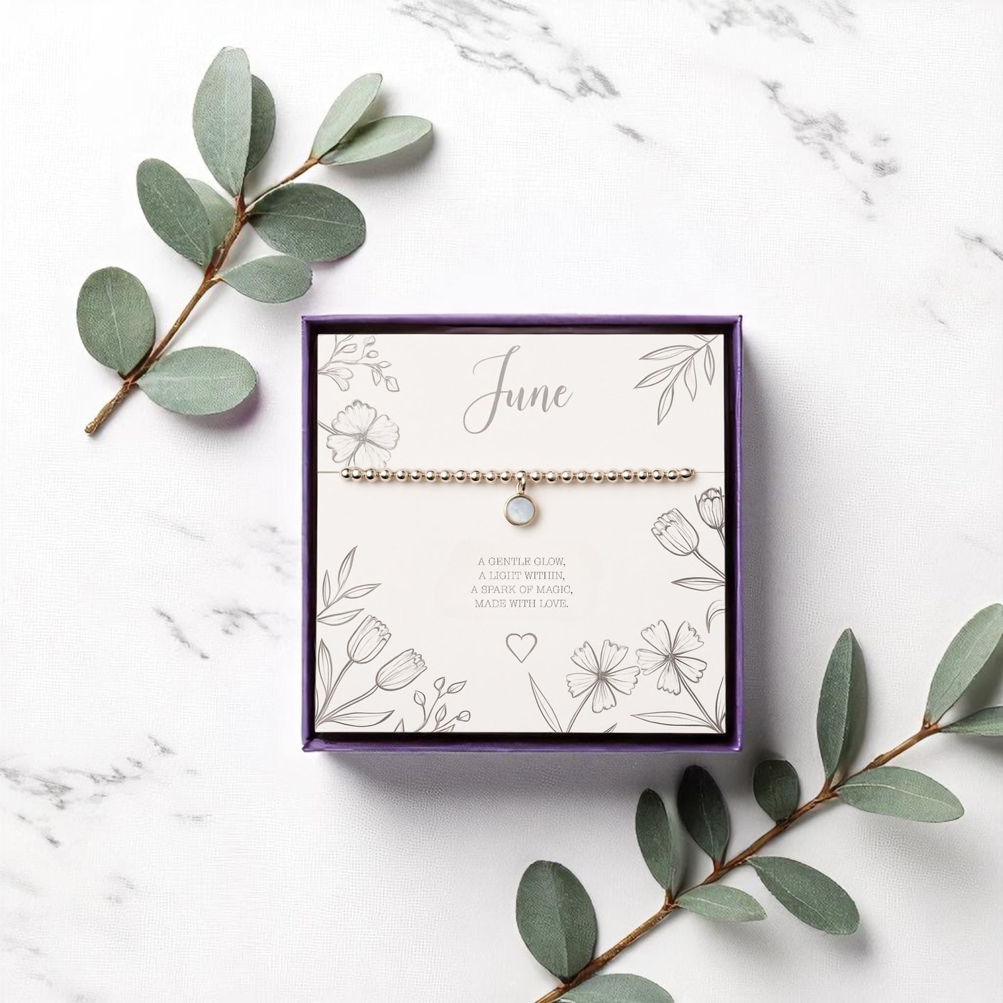 Handmade June birthstone charm bracelet featuring a delicate moonstone charm on a stretch bead bracelet with gold accents. Displayed on a floral message card in a purple gift box, this calming crystal bracelet is a meaningful gift for her.