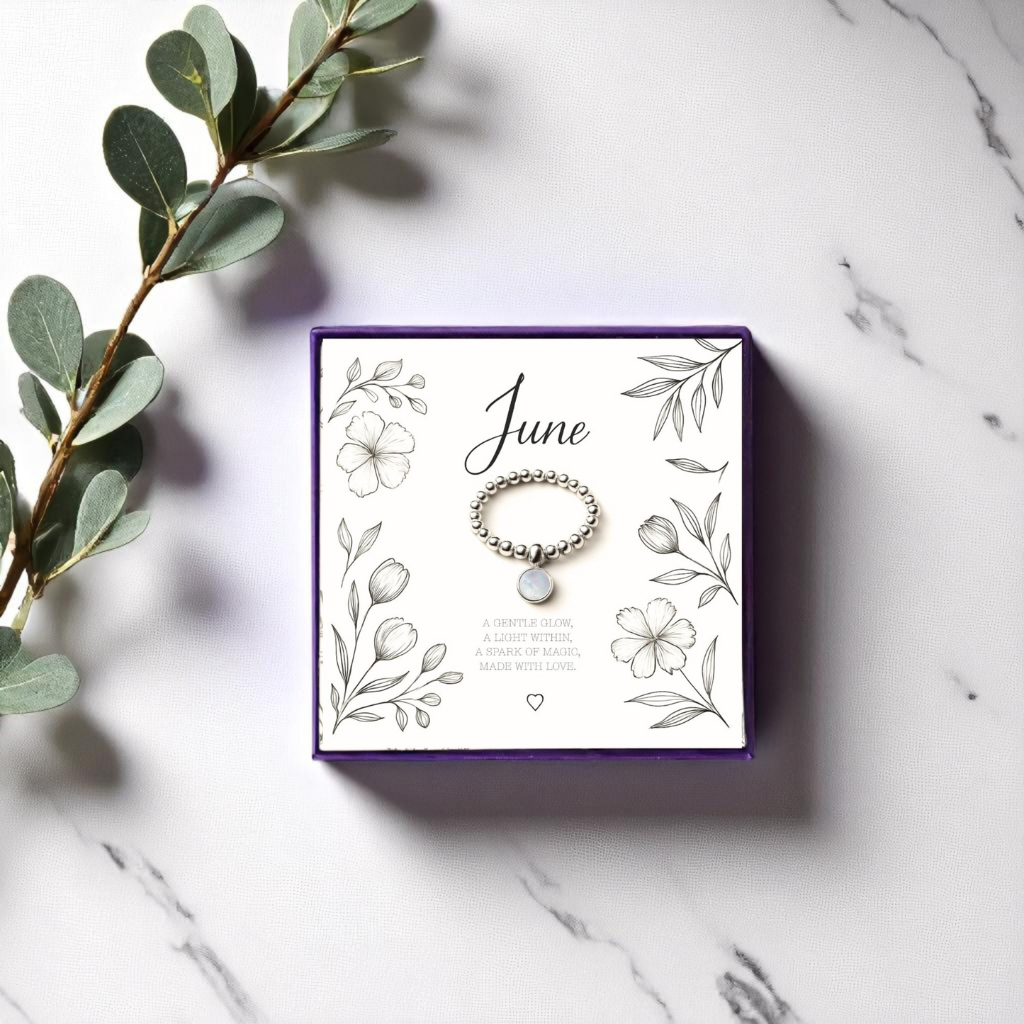 Handmade June birthstone stretch ring featuring a shimmering moonstone charm and silver bead band. Displayed on a floral message card in a purple gift box, this dainty crystal ring is a meaningful gift and calming piece of gemstone jewellery