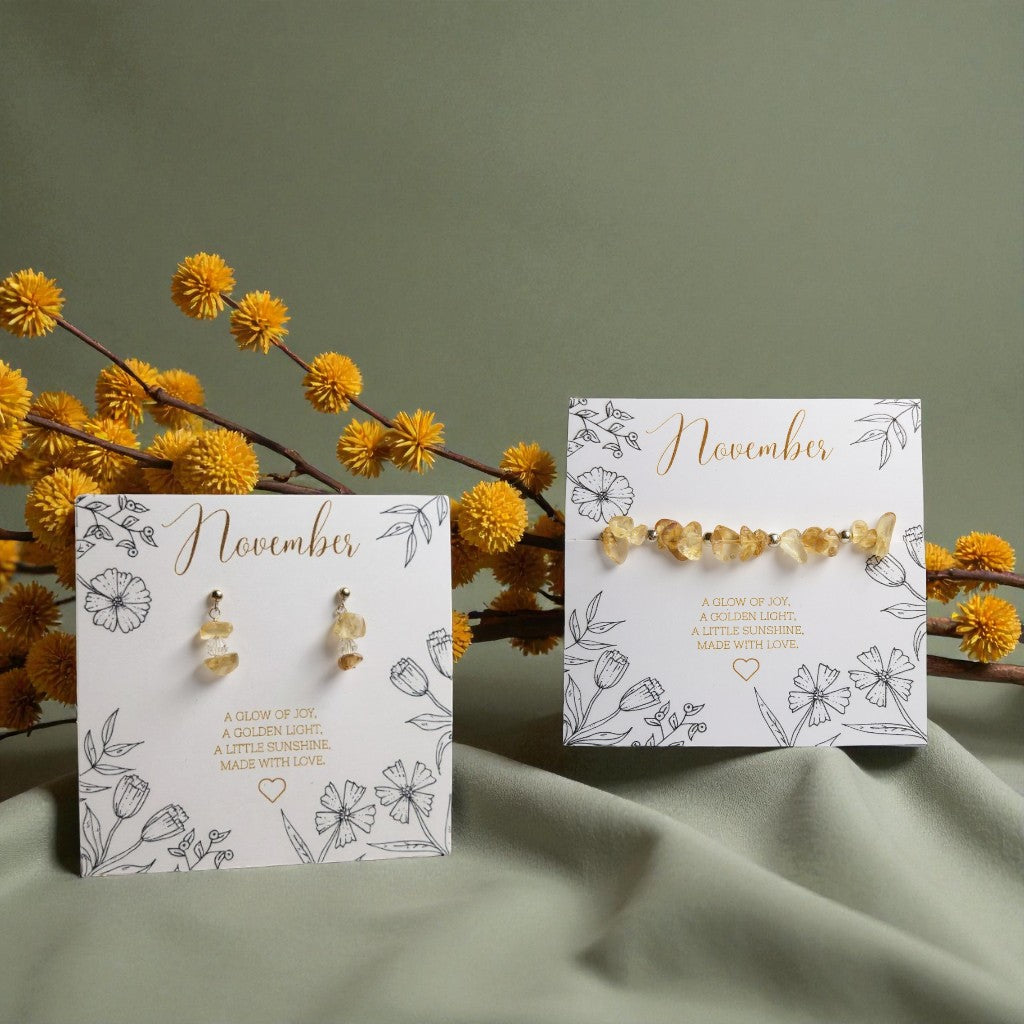 November citrine birthstone earrings and bracelet displayed on floral illustrated cards reading ‘A glow of joy, a golden light, a little sunshine. Made with love.’ Set against a soft green fabric backdrop with yellow flowers