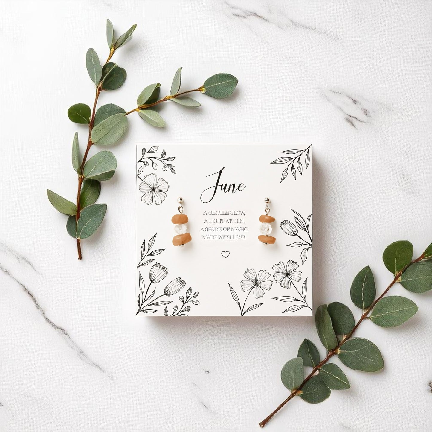 Handmade June birthstone earrings featuring stacked peach moonstone and crystal beads on silver hooks, displayed on a floral message card. A meaningful gemstone gift for her, styled with eucalyptus on a marble background.