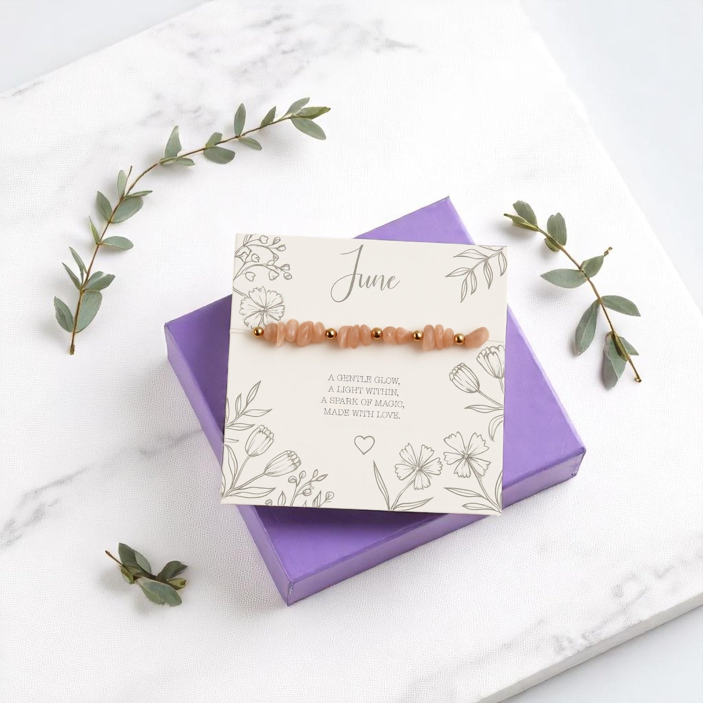 June birthstone stretch bracelet with peach moonstone crystal chips and gold accents, displayed on a floral message card atop a purple gift box. A handmade gemstone bracelet and meaningful birthday gift for he