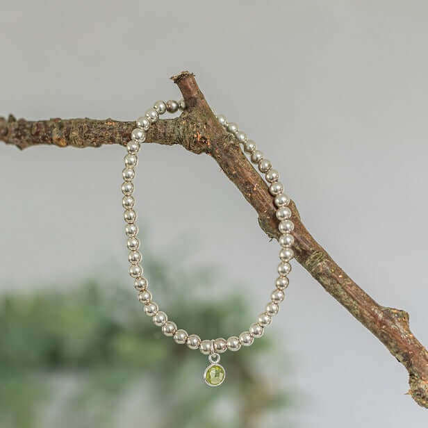 Peridot August birthstone charm bracelet hanging on branch with sterling silver beads