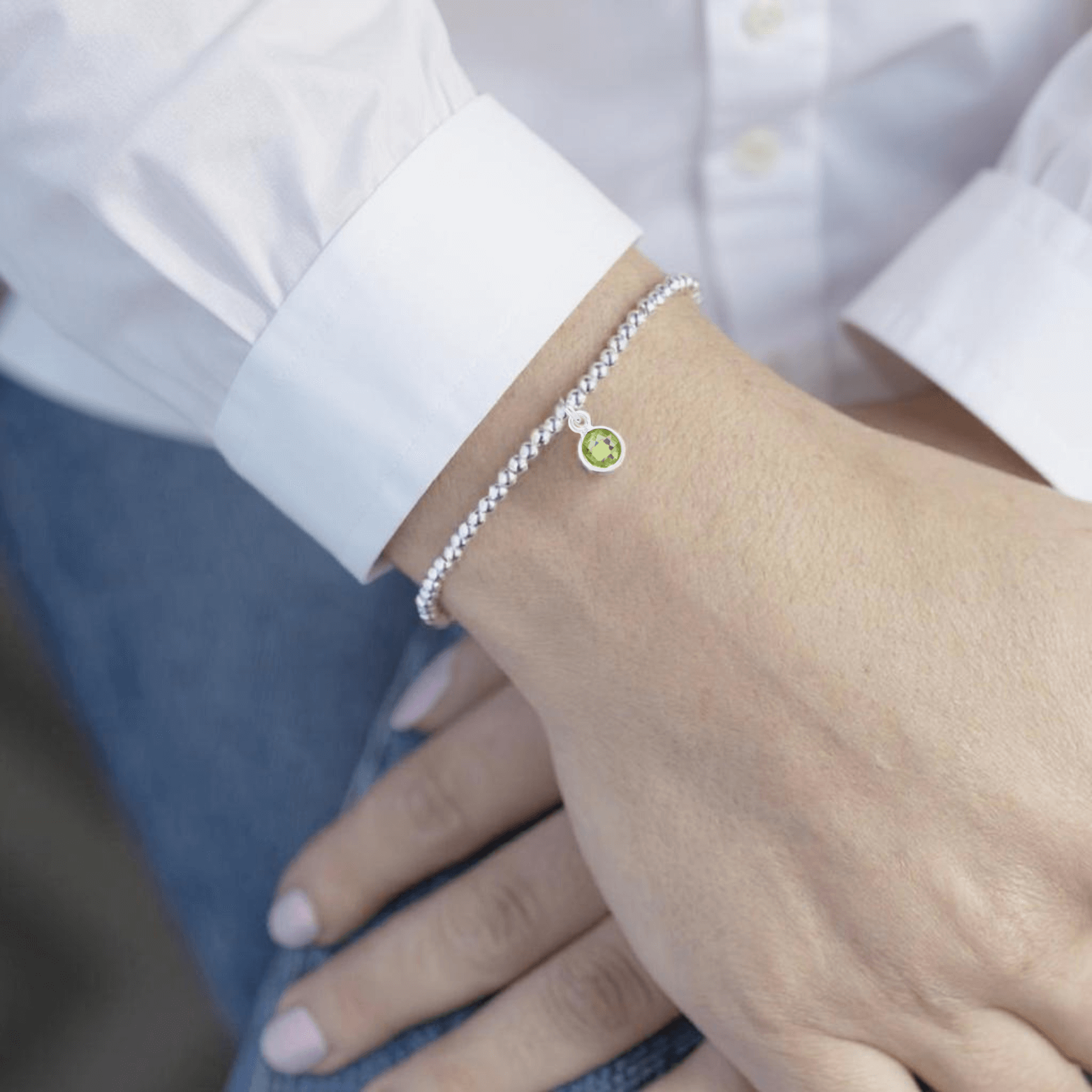 Sterling silver peridot charm bracelet worn on wrist with white cuff shirt