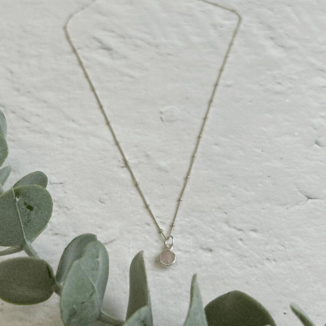 Close-up of Rose Quartz Birthstone Necklace on sterling silver chain with gemstone charm, displayed on white stone surface