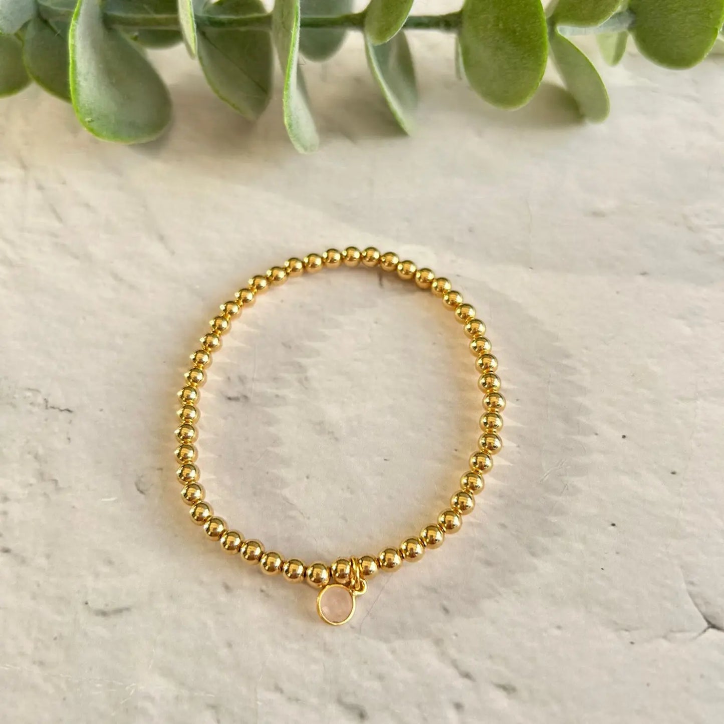 Gold filled Rose Quartz Charm Bracelet with gemstone charm displayed on stone background with eucalyptus