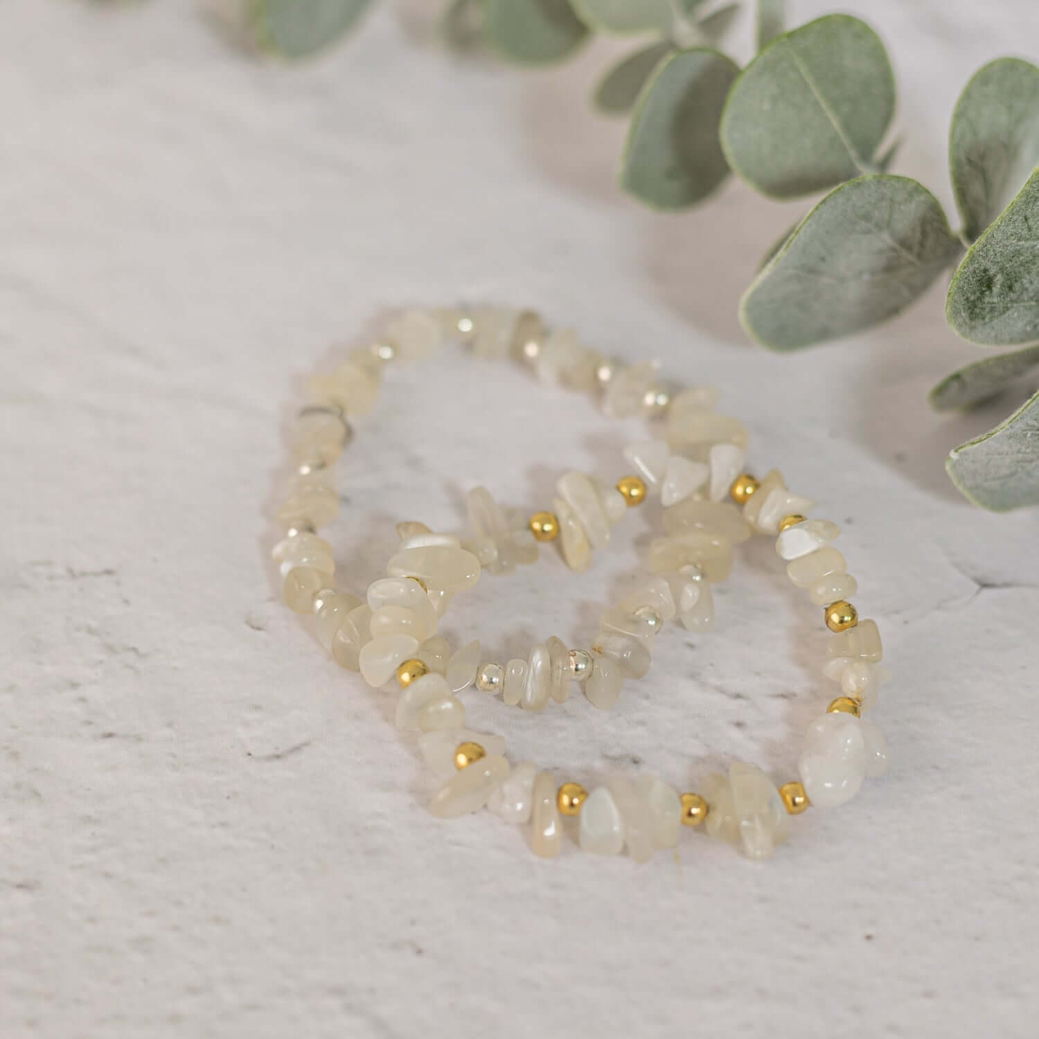 A close-up of two beaded bracelets featuring light-colored gemstones showcasing elegant birthstone jewellery for June. Placed on a light surface with eucalyptus leaves in the background, the bracelets are arranged in a slightly overlapping fashion.