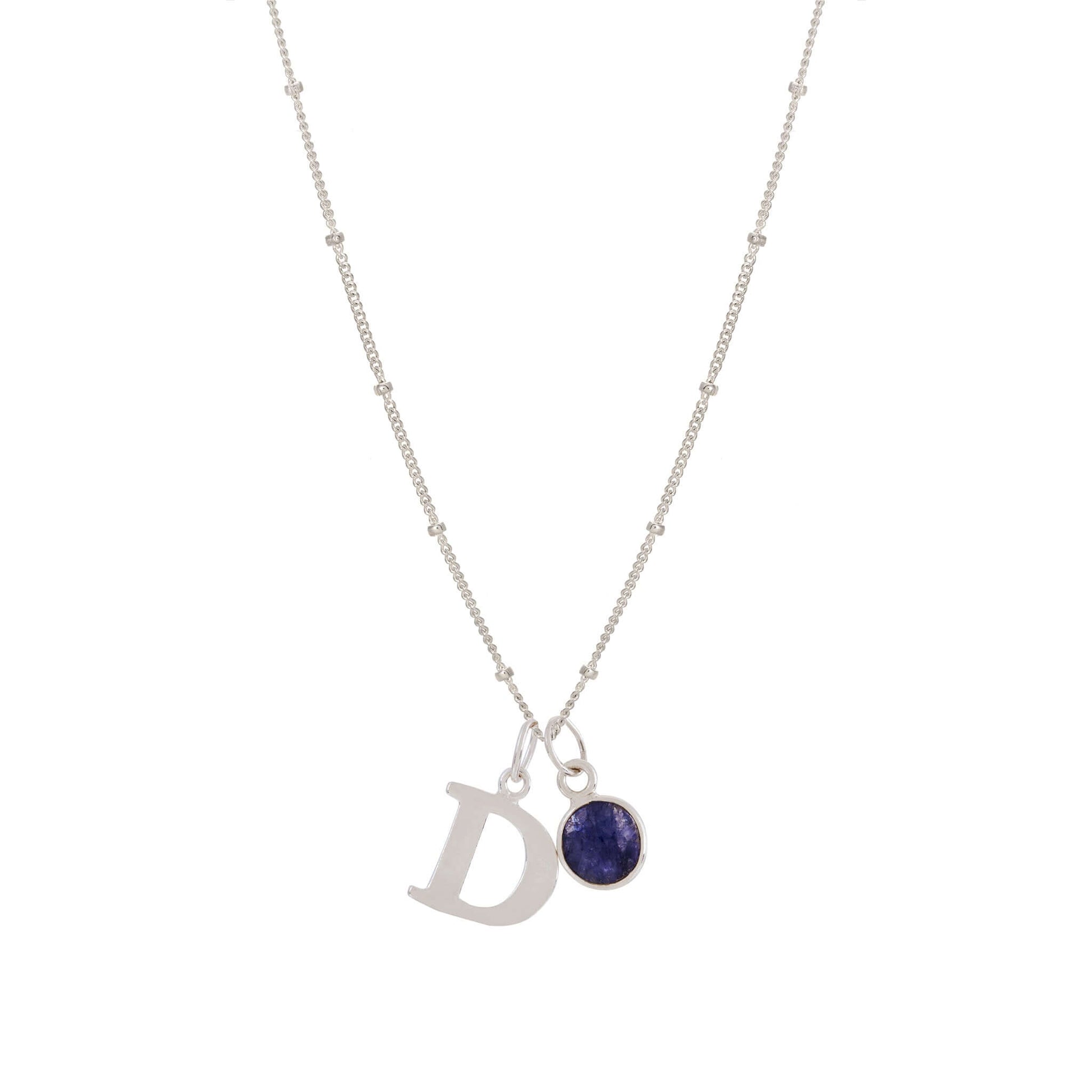 Introducing the Initial Letter & Birthstone Charm Necklace by Made Here with Love: A delicate 925 sterling silver chain featuring two pendants—one silver letter "D" and a round Birthstone Charm in a silver setting. The fine necklace chain boasts small bead details spaced throughout, with the pendants positioned near its center.