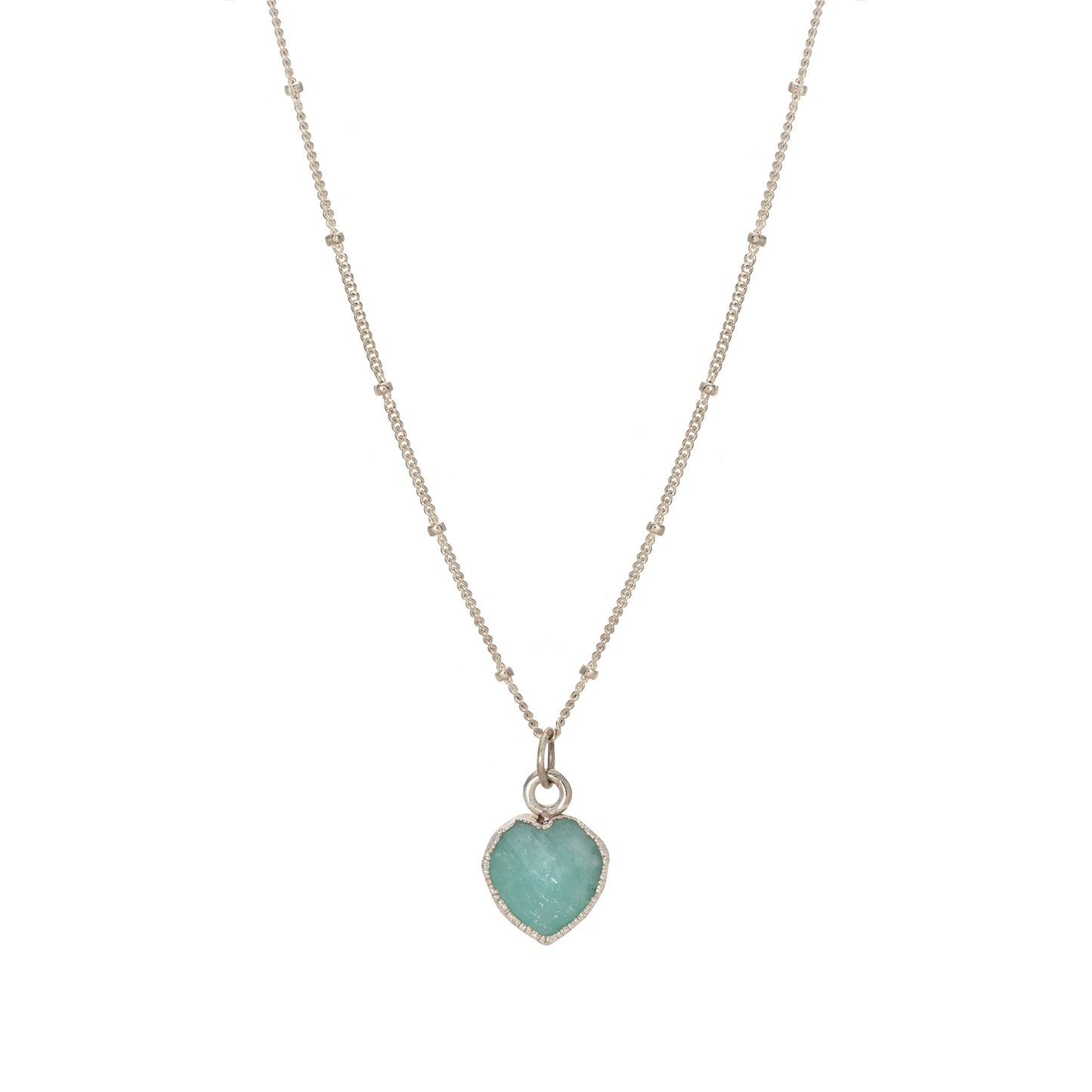 The **Heart Charm Necklace** by **Made Here with Love** features a thin sterling silver chain adorned with tiny beads. The pendant is a small, heart-shaped turquoise stone encased in a gold setting. The design is simple yet elegant, perfect for a subtle touch of color and charm.