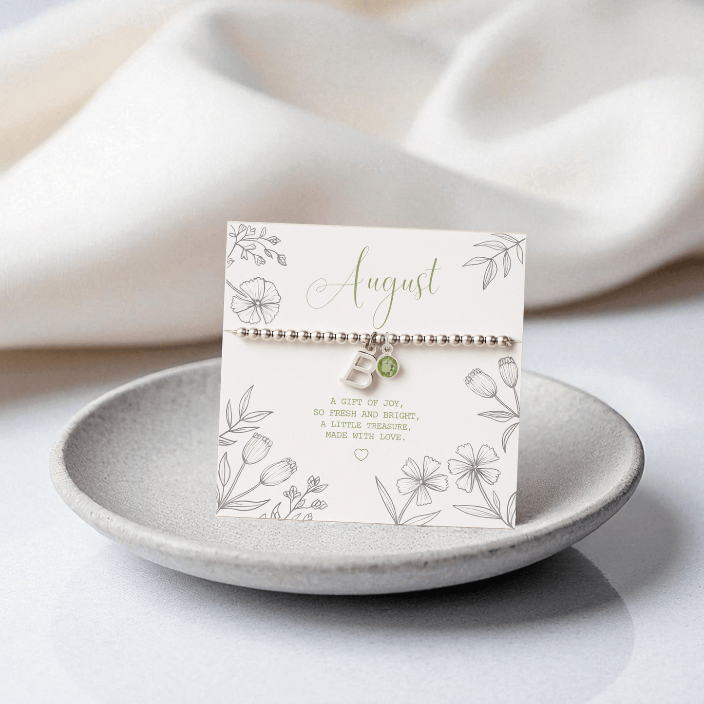 Sterling silver initial and peridot August birthstone bracelet displayed on gift card with floral design in neutral setting