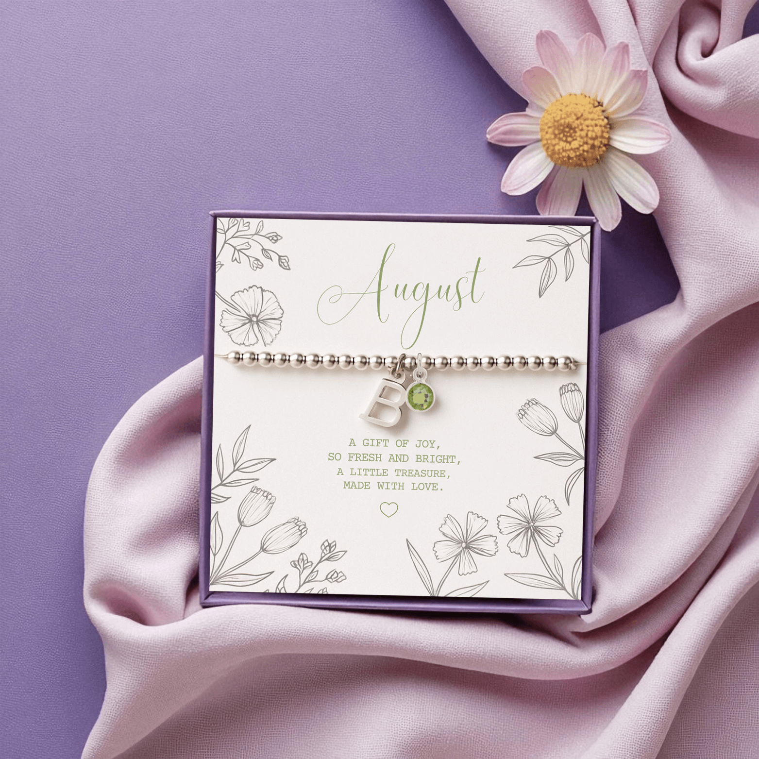 Initial & August Birthstone Bracelet with peridot charm shown on purple satin backdrop beside daisy and ribbon
