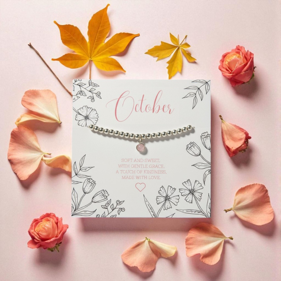 Rose Quartz Charm Bracelet presented on October birthstone card with autumn leaves and pink flower petals