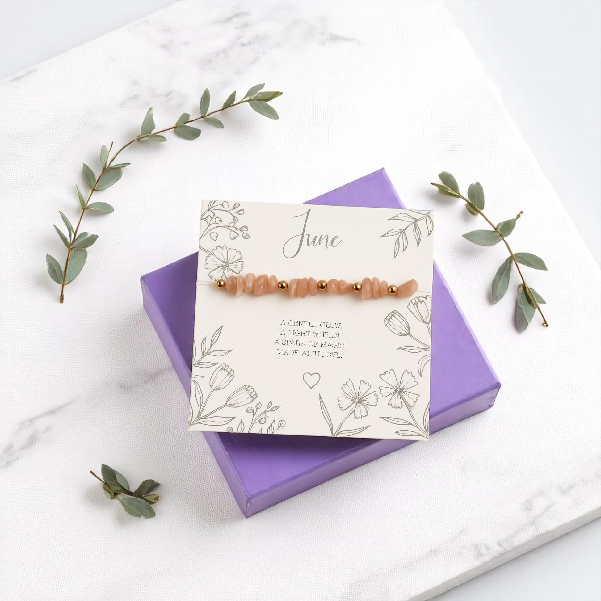 June birthstone stretch bracelet with peach moonstone crystal chips and gold accents, displayed on a floral message card atop a purple gift box. A handmade gemstone bracelet and meaningful birthday gift for he