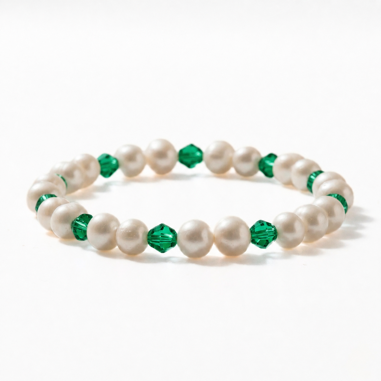 A stretch beaded bracelet alternating creamy freshwater pearls with vivid faceted emerald green bicone crystals throughout, on a white background