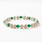 A stretch beaded bracelet alternating creamy freshwater pearls with vivid faceted emerald green bicone crystals throughout, on a white background