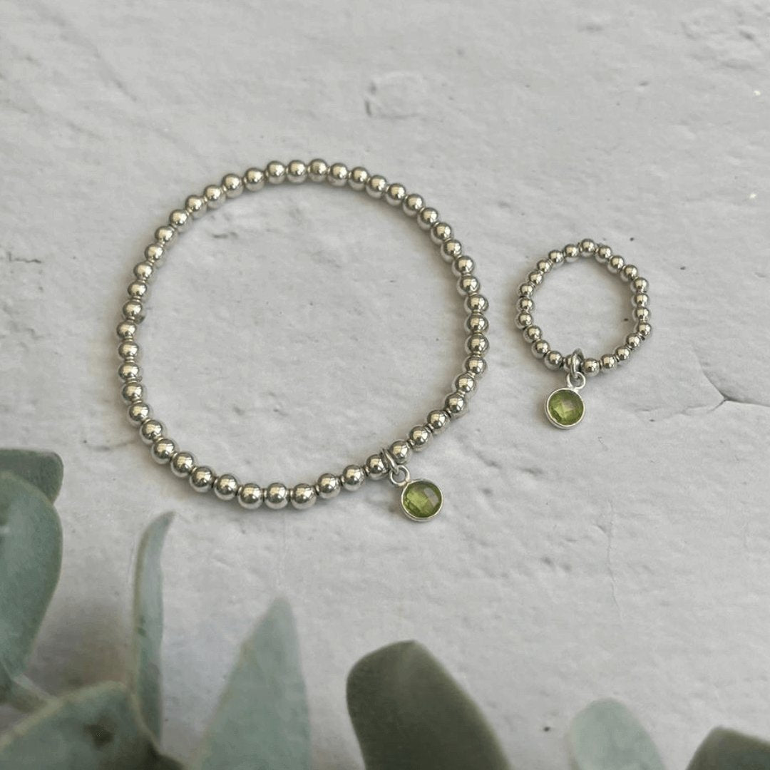 Peridot birthstone bracelet and ring set with sterling silver beads on stone background