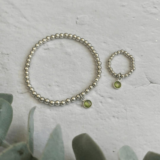 Peridot birthstone bracelet and ring set with sterling silver beads on stone background