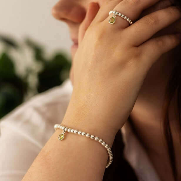 Peridot charm bracelet styled on wrist with matching peridot birthstone charm ring