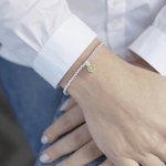 Sterling silver peridot charm bracelet worn on wrist with white cuff shirt