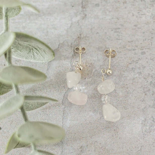 Rose Quartz Drop Earrings with sterling silver accents, displayed on light stone background with soft green foliage.