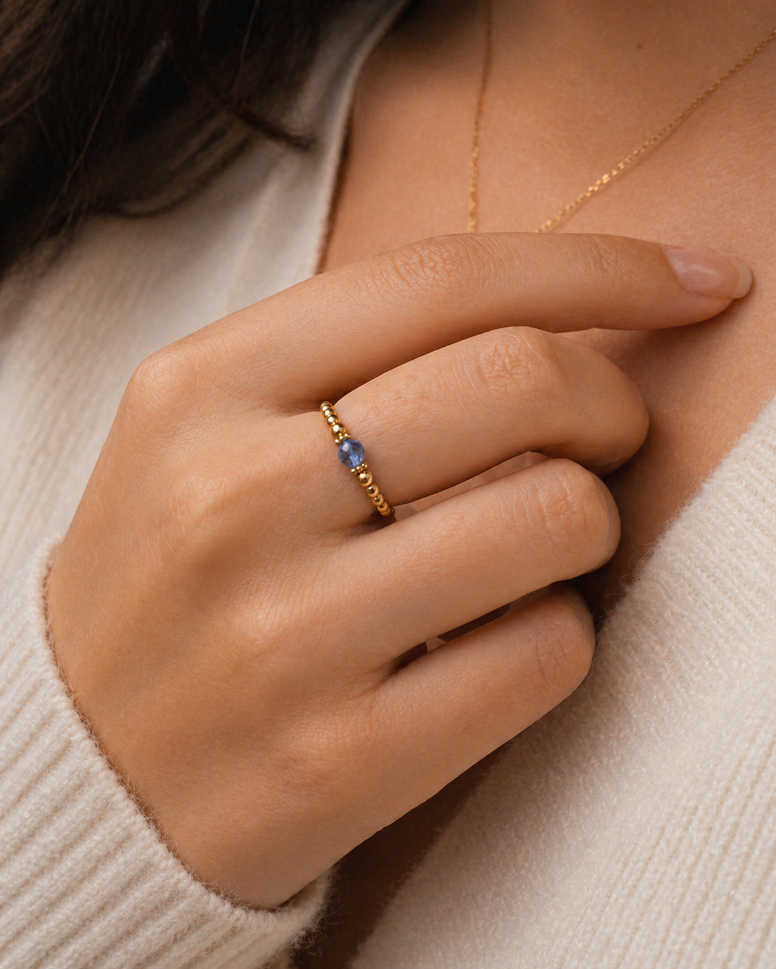 Close-up of a hand wearing a gold ring with a blue gemstone, against a neutral background.