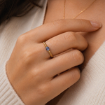 Close-up of a hand wearing a gold ring with a blue gemstone, against a neutral background.