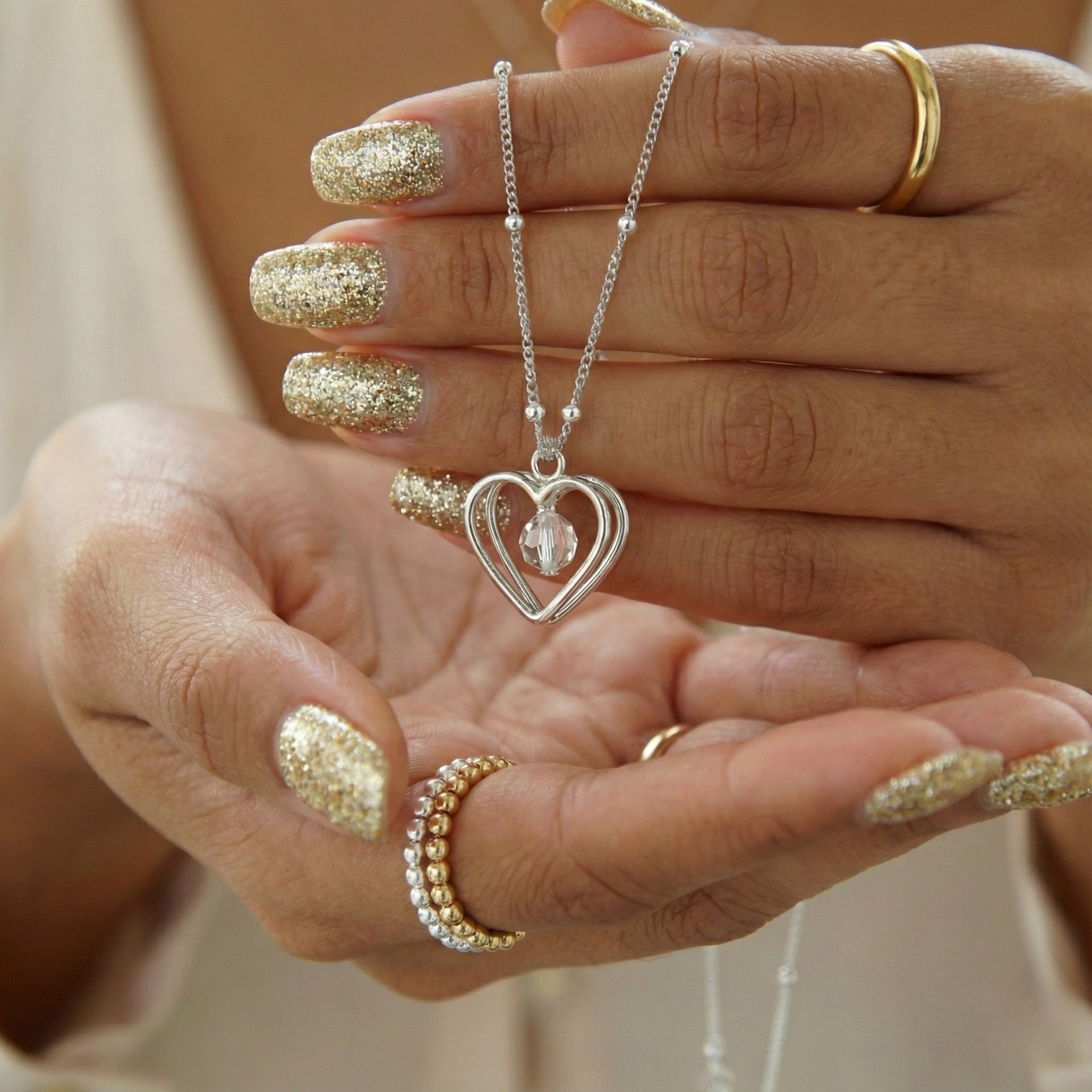 Sterling silver open heart necklace with crystal bead detail, held in hand.